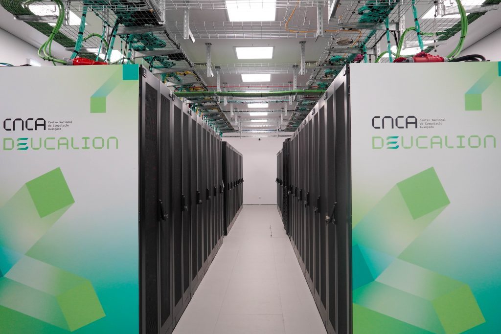 Corredor do supercomputador Deucalion, com filas de armários de servidores e o logótipo do Centro Nacional de Computação Avançada